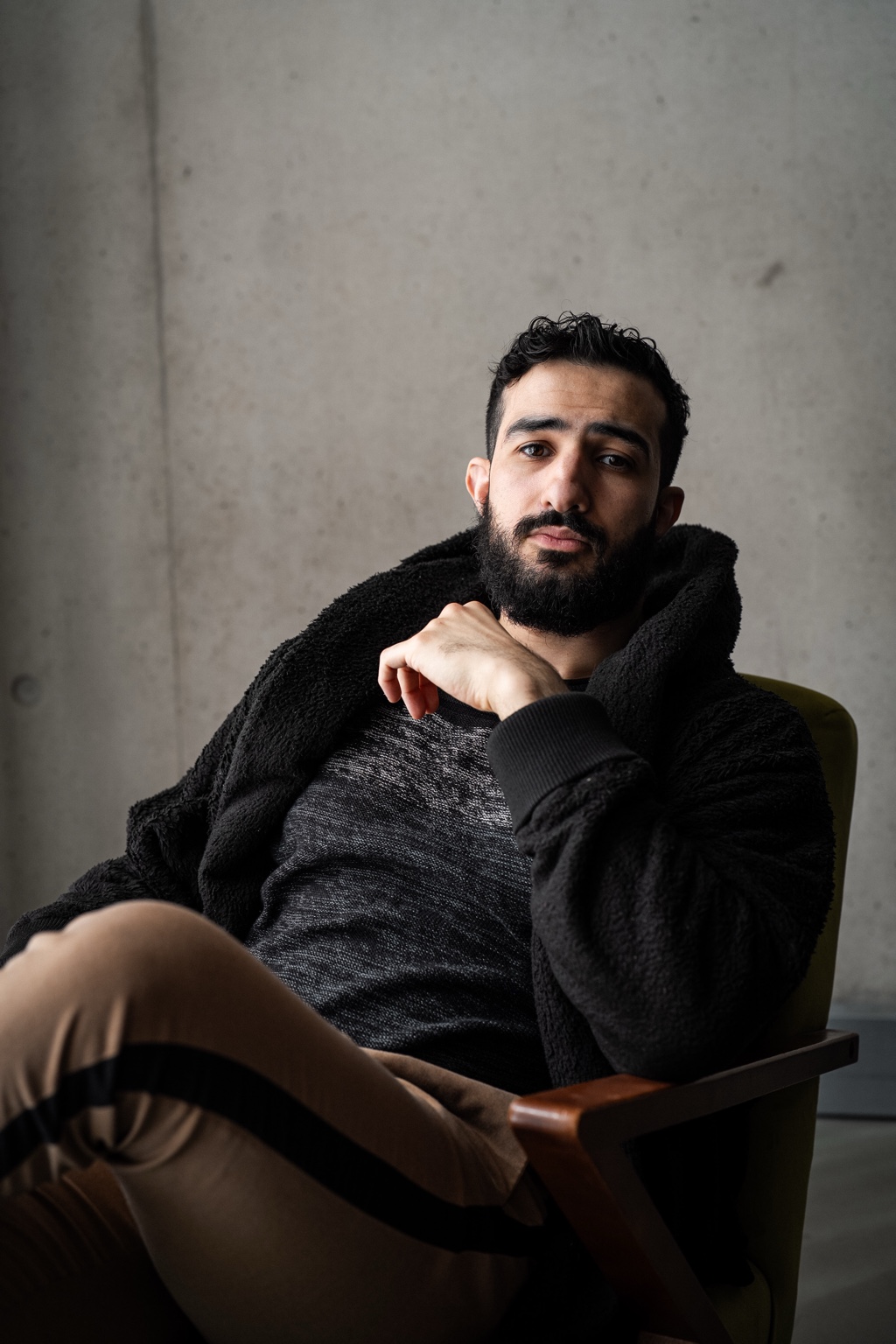 Mohamed Chahrour: Seated portrait in a dark coat, against a concrete wall